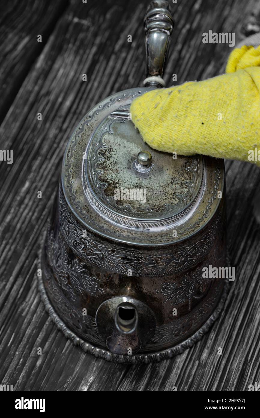 Cleaning antique tarnished silver teapot with a yellow duster. On a