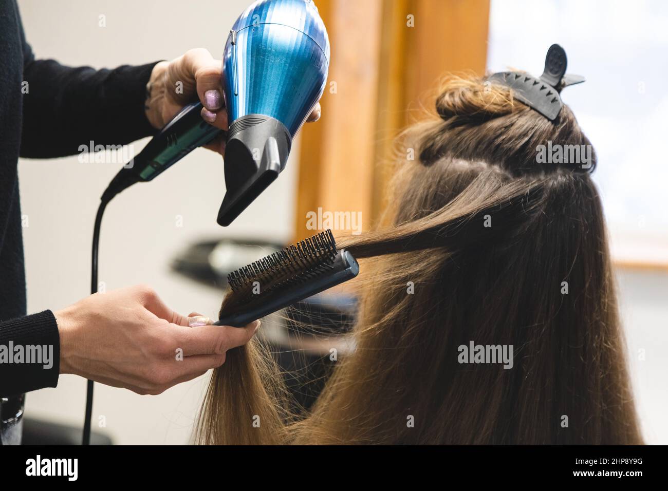 Master woman hairdresser dries the girl's hair with a hairdryer and