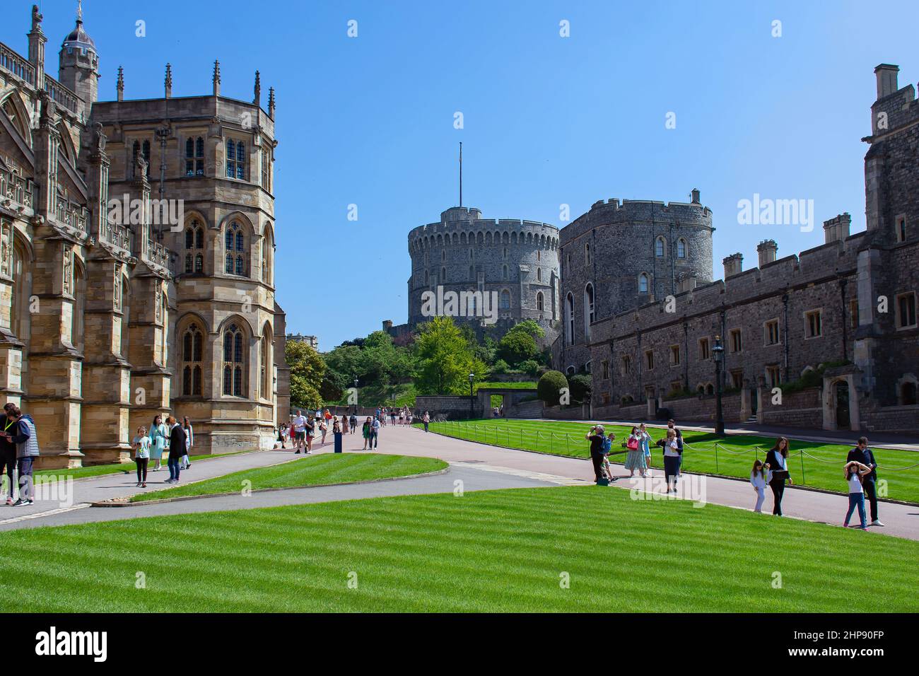 Visitors walk on the pathways next to St Georges Chapel in the Lower Ward of Windsor Castle, UK.  The Round Tower can be seen looming above the path. Stock Photo