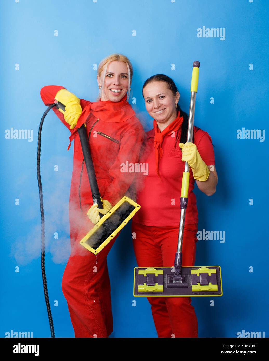 Two female cleaning company workers in red uniforms smile against an