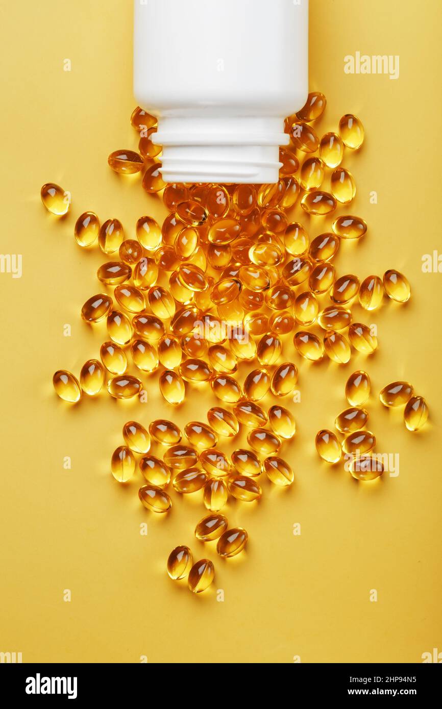 Golden Omega-3 fish oil capsules poured out of a jar on a yellow  background. Free space Stock Photo - Alamy