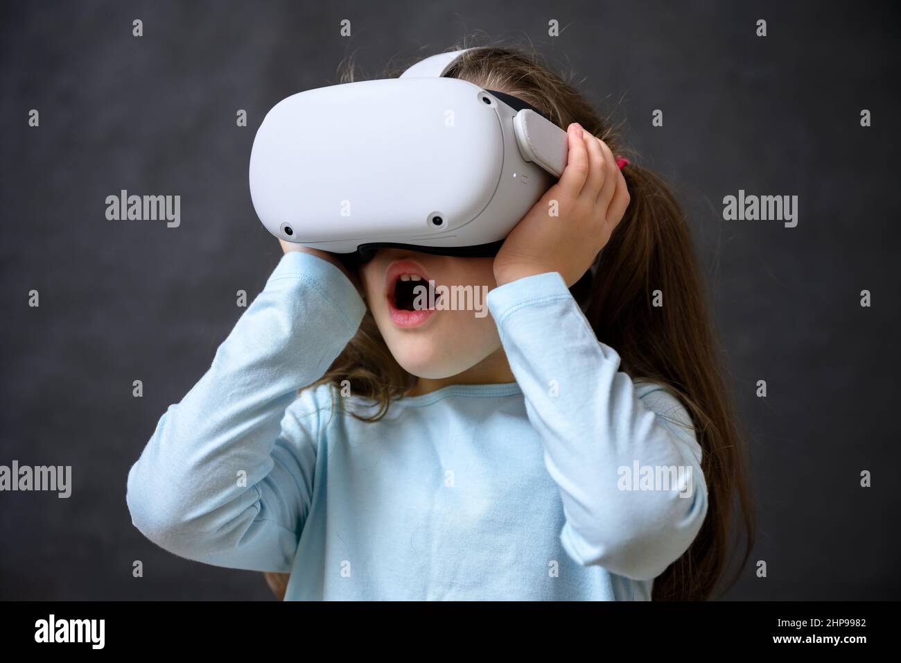 Kid using virtual reality headset, surprised child looking in VR glasses. Young person with futuristic goggles having fun, little girl playing video g Stock Photo