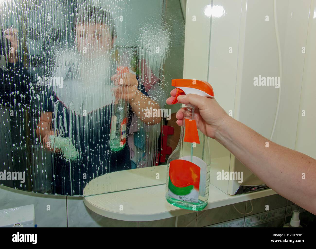 A woman cleans a mirror with a napkin from dirt and plaque from water