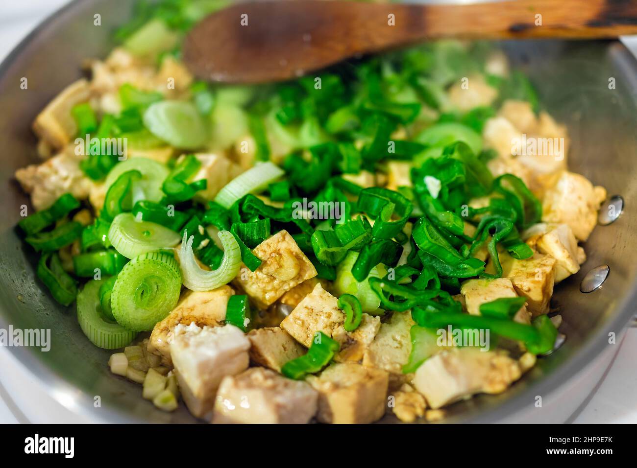Tofu cubes frying in stainless steel pan with green onion chopped negi