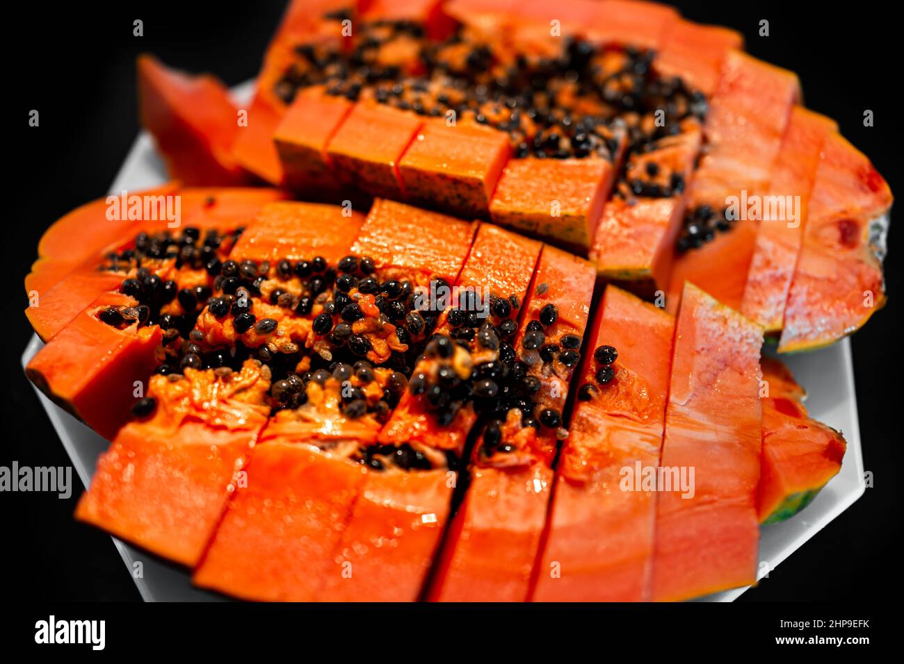 Closeup macro of large Caribbean red ripe papaya fruit sliced two halves slices with fresh orange red colorful flesh cut in half on plate with black b Stock Photo