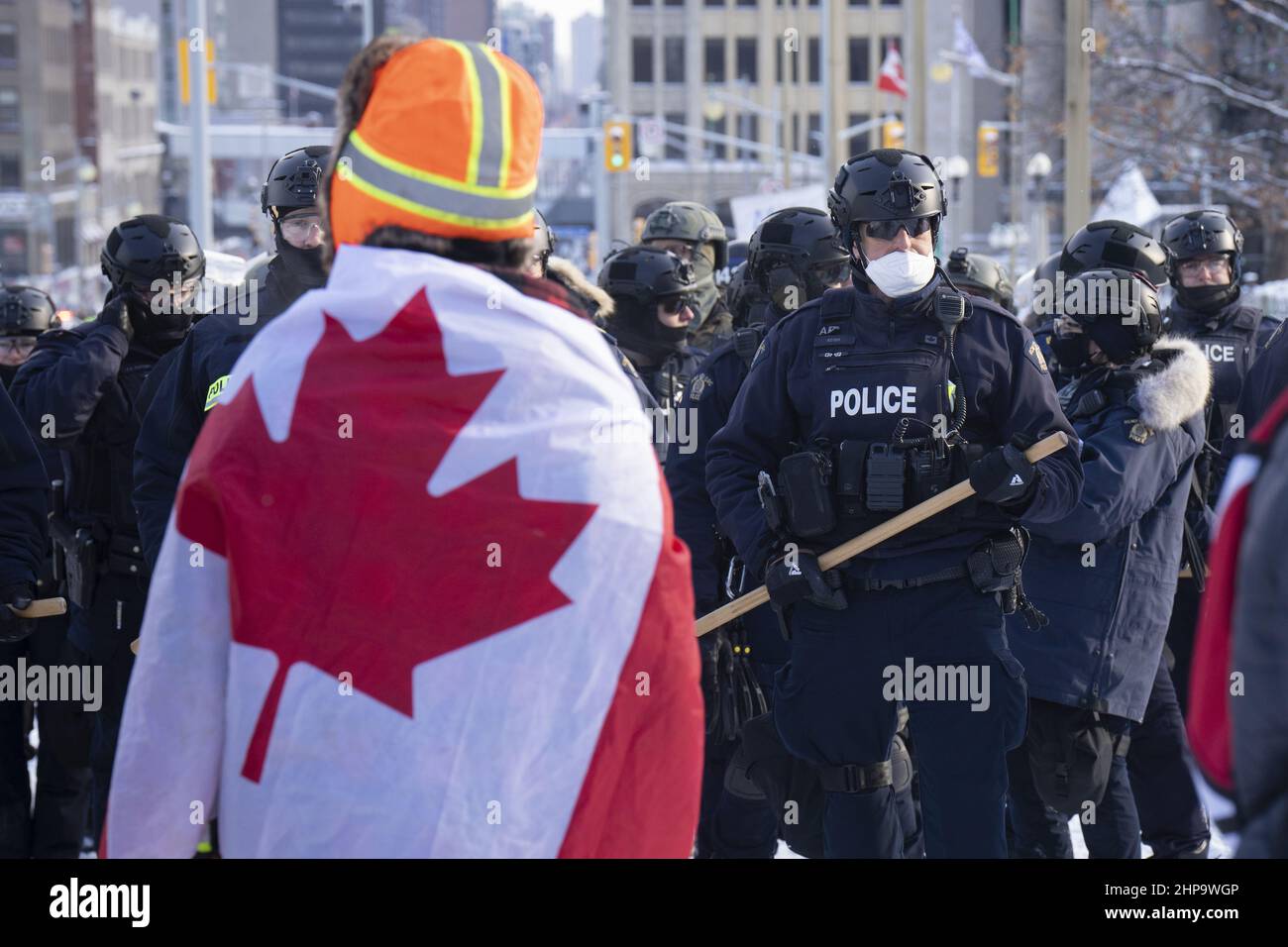 A police officer in Ottawa holds a baton in front of a Freedom Convoy protestor draped in a Canada flag as they prepare to drive them out of the area. Stock Photo