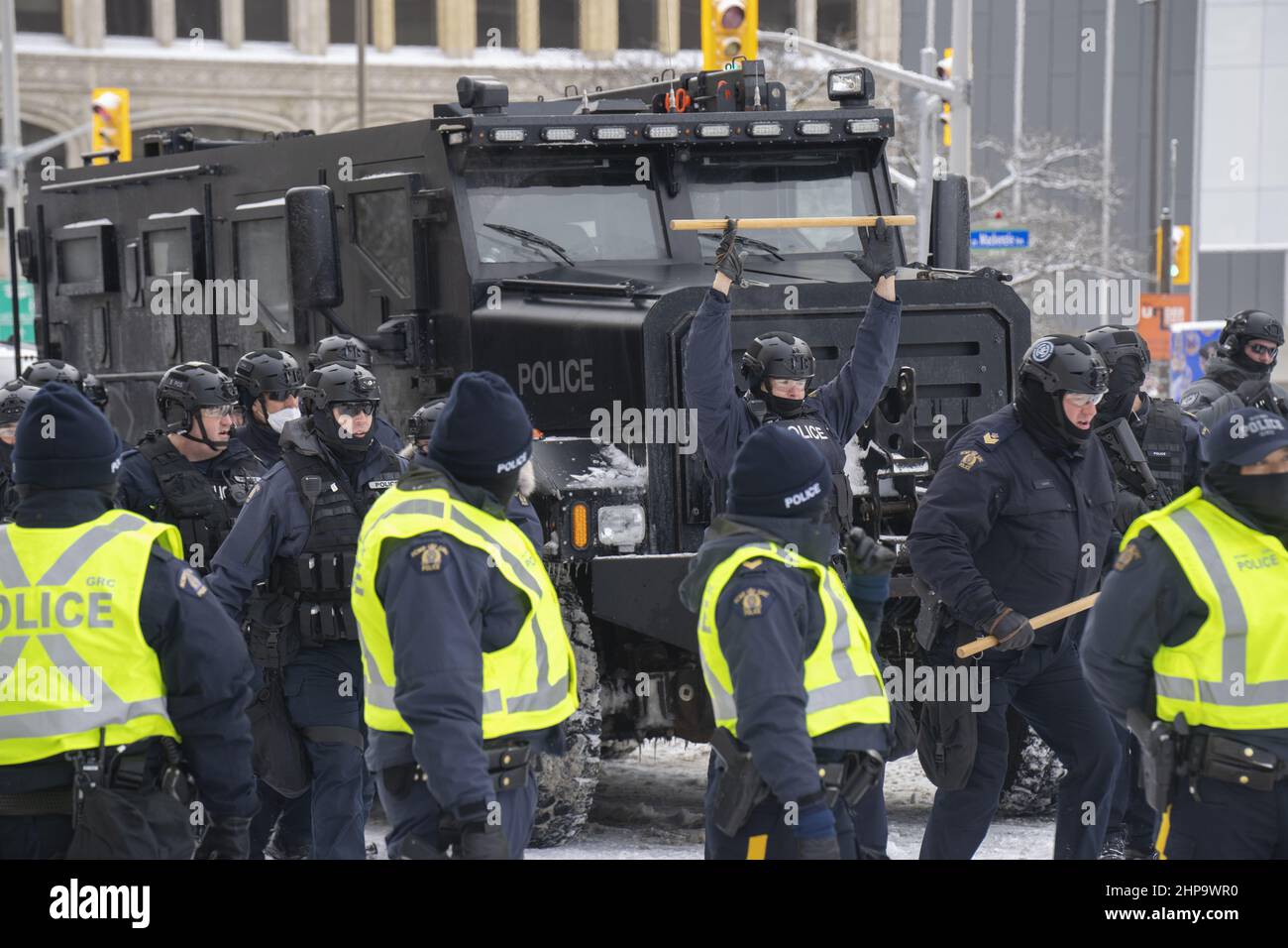 A police officer holds a baton up in front of an armored vehicle as police get ready to drive out Freedom Convoy protestors in Ottawa on Feb 19, 2022 Stock Photo
