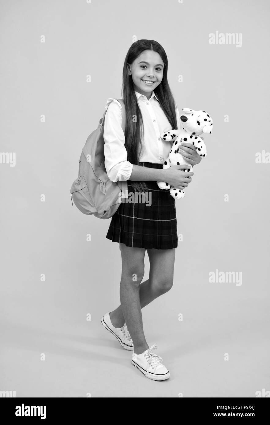 cheerful teen girl with backpack in school uniform full length on yellow background, school time. Stock Photo
