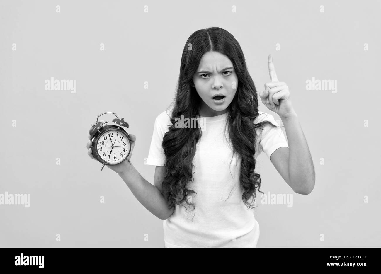 serious kid hold retro alarm clock showing time with raised finger, discipline Stock Photo