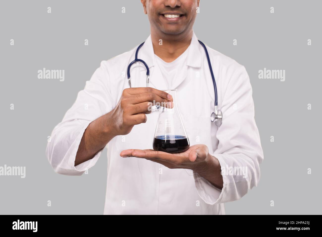 Male Doctor Showing Flask with Colorfull Liquid Isolated Close Up. Science, Medical, Virus Concept. Indian Man Doctor Smilling. Stock Photo