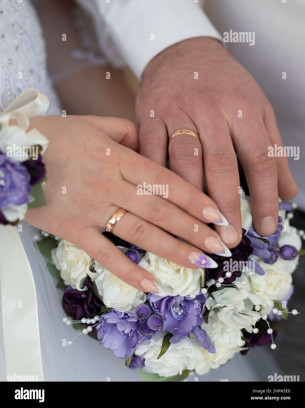 Hands of the groom and the bride on a wedding bouquet Stock Photo