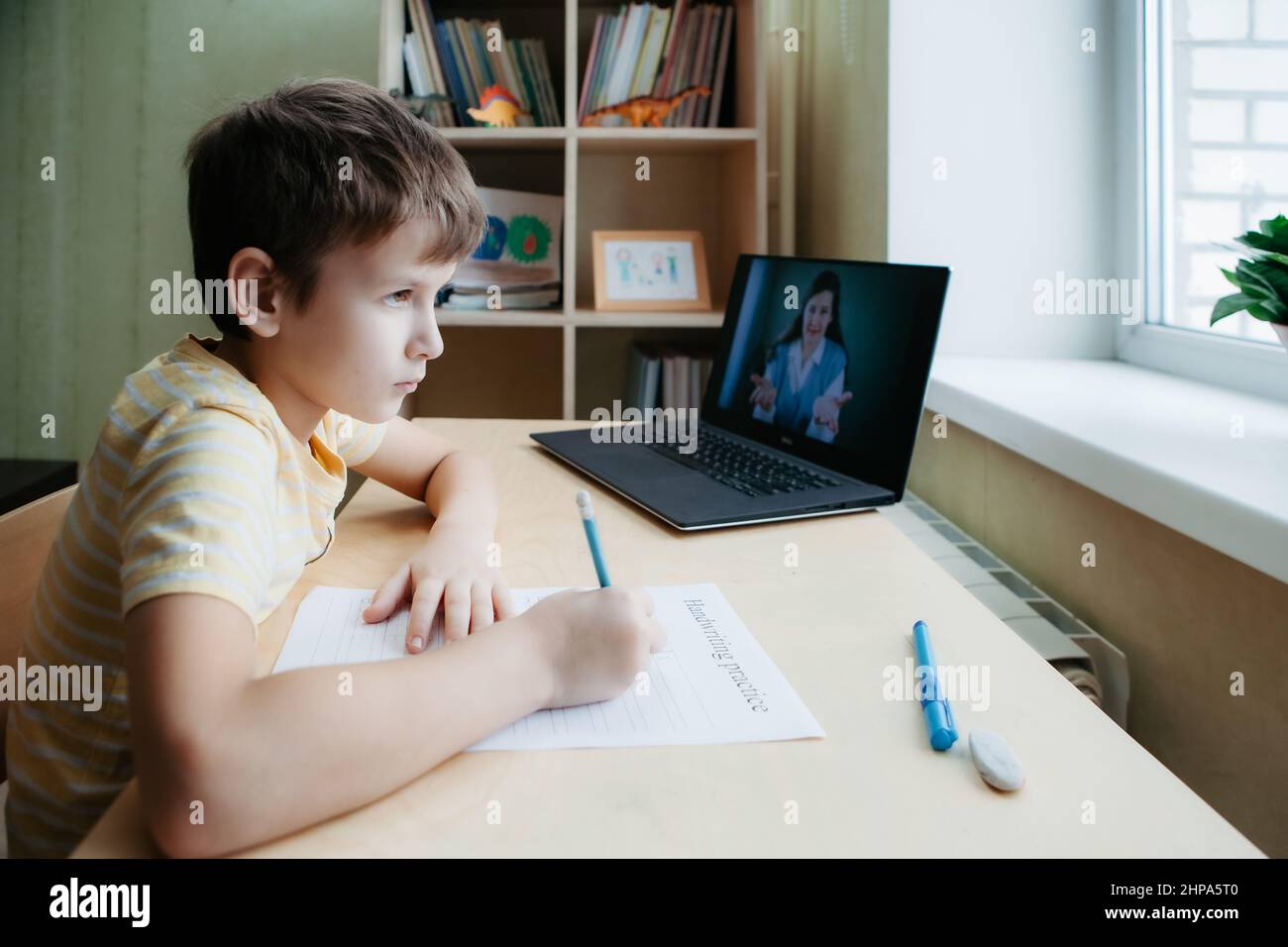 8 years old boy sit by desk with laptop and do writing task during