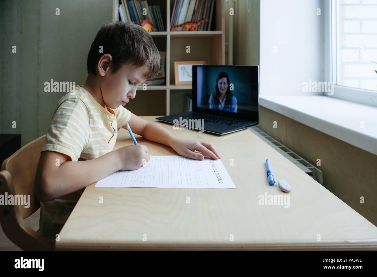 8 years old boy sit by desk with laptop and do writing task during