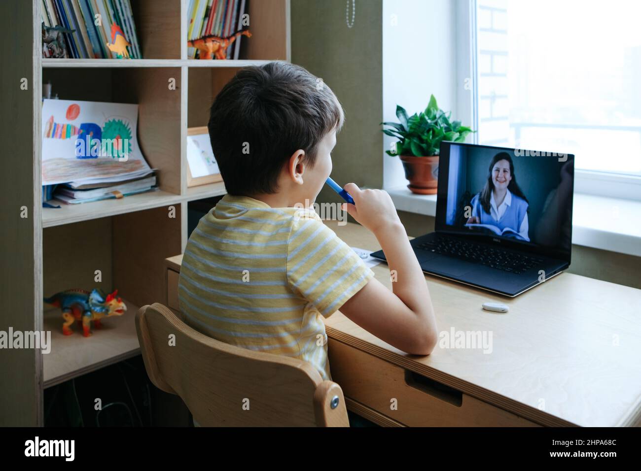 8 years old boy sit by desk with laptop and do writing task during