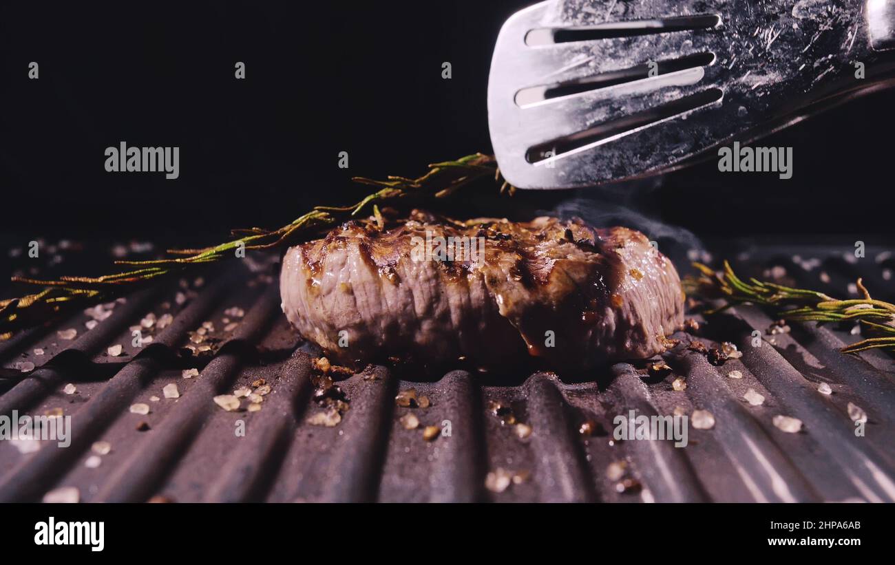 Delicious juicy meat steak cooking on grill. Kitchen tongs. Aged prime rare roast grilling