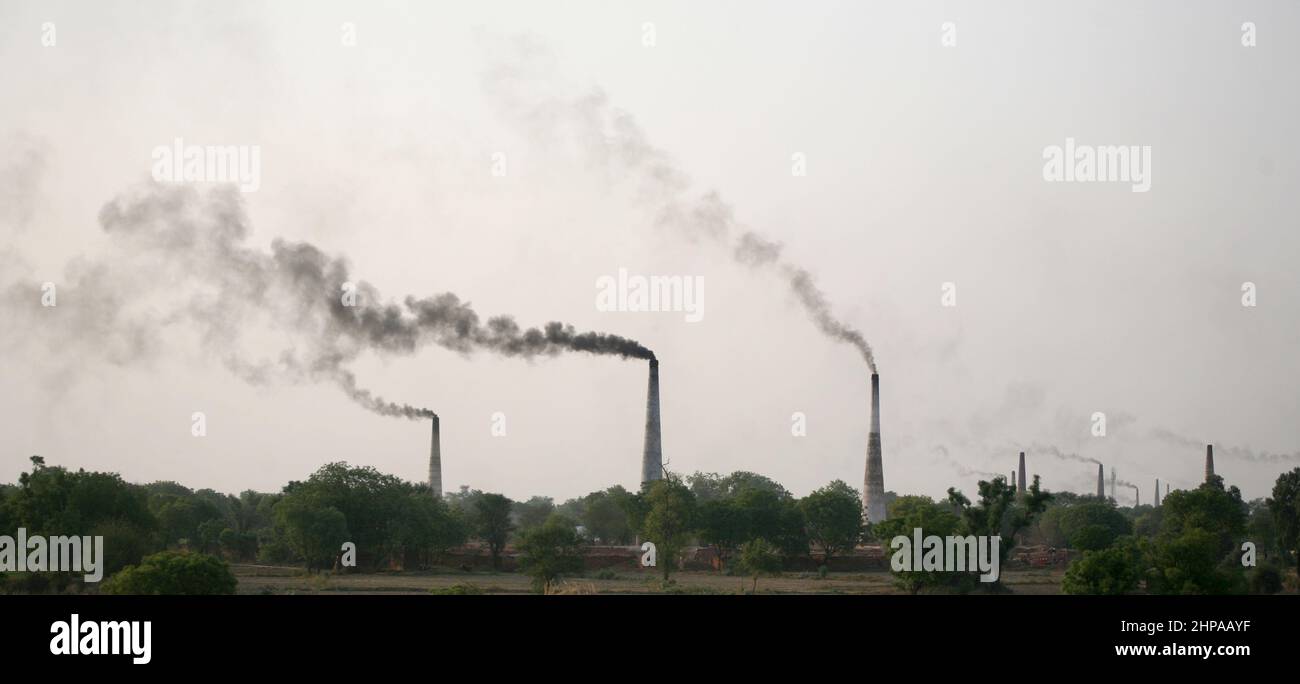 Thick black smoke rise from the coal fueled chimney of the Brick Kiln near Mathura district in Uttar Pradesh in India. Stock Photo
