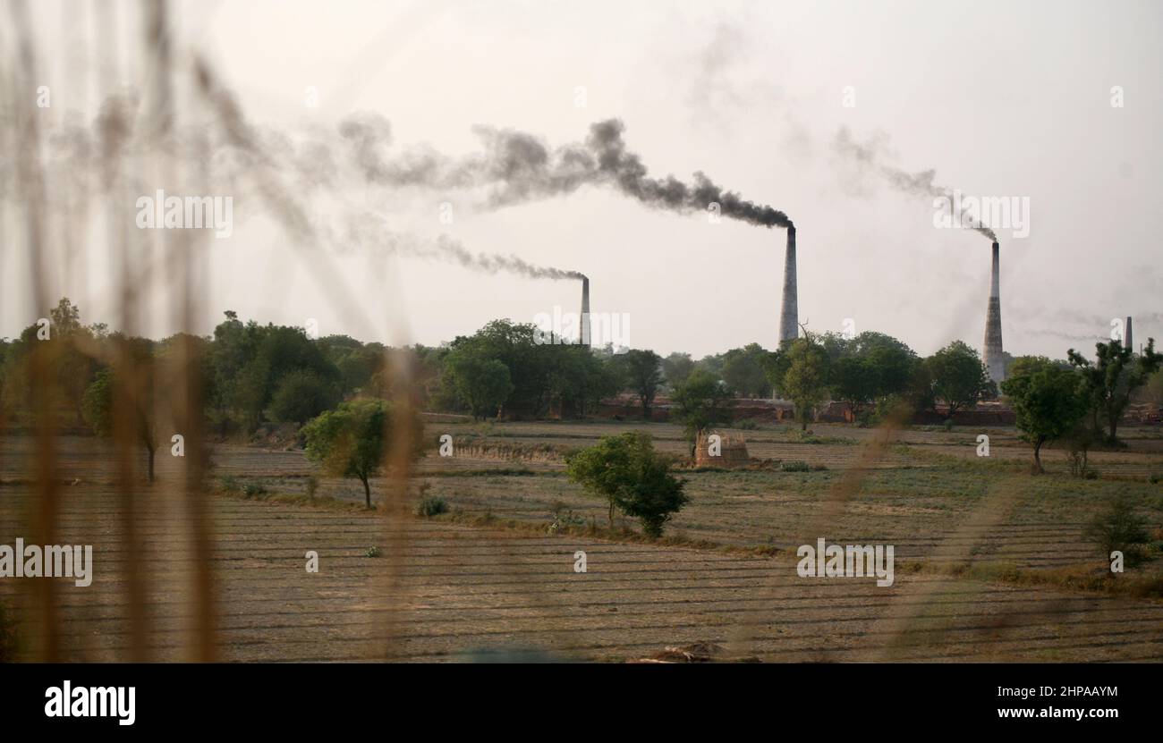 Thick black smoke rise from the coal fueled chimney of the Brick Kiln near Mathura district in Uttar Pradesh in India. Stock Photo