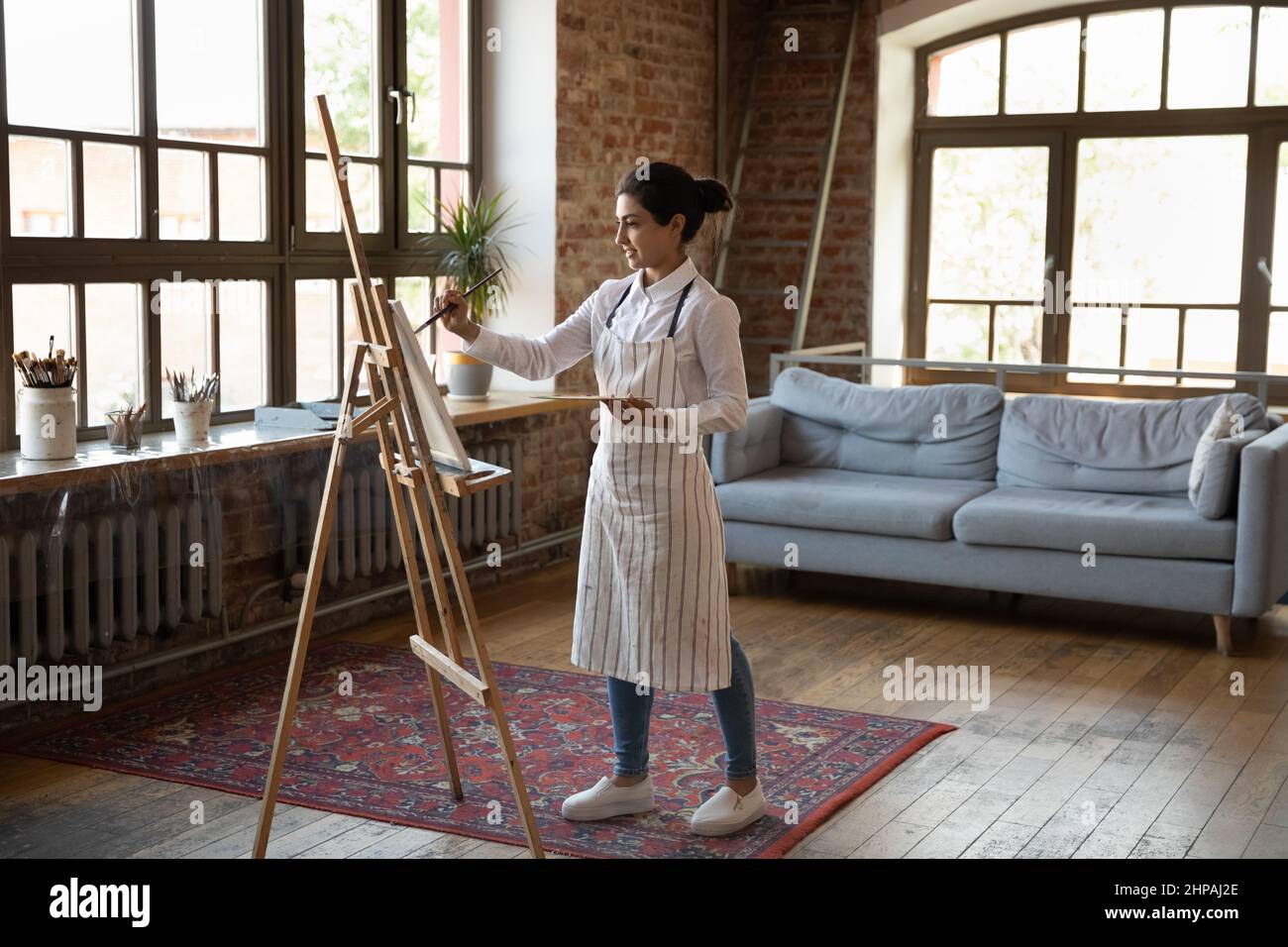 Full length creative millennial Indian woman drawing on easel. Stock Photo