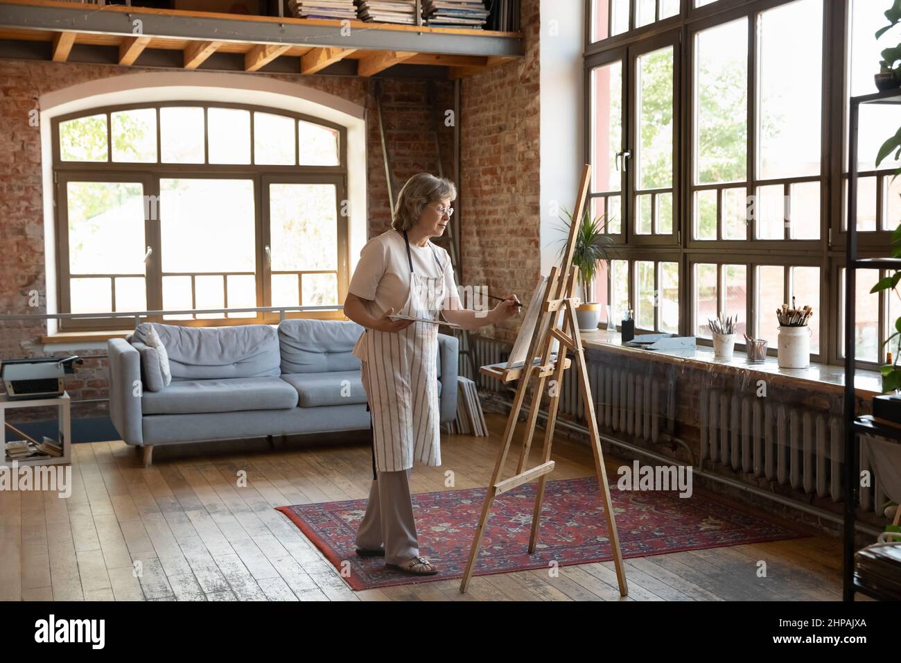 Focused happy old senior retired woman drawing on easel. Stock Photo
