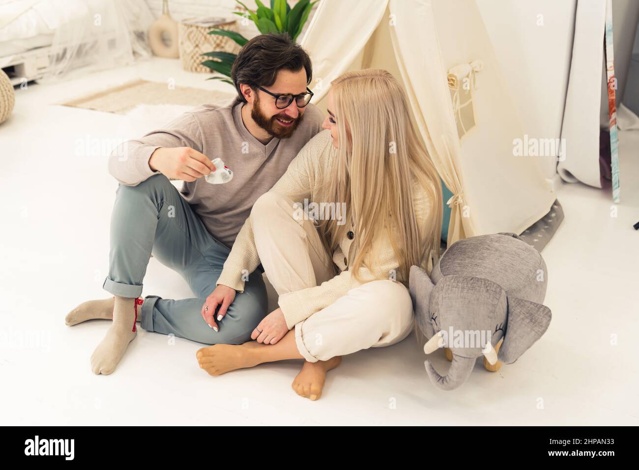 soon-to-be parents in their late 20s sitting in a baby's room, holding little infant shoe, and talking about the future. High quality photo Stock Photo