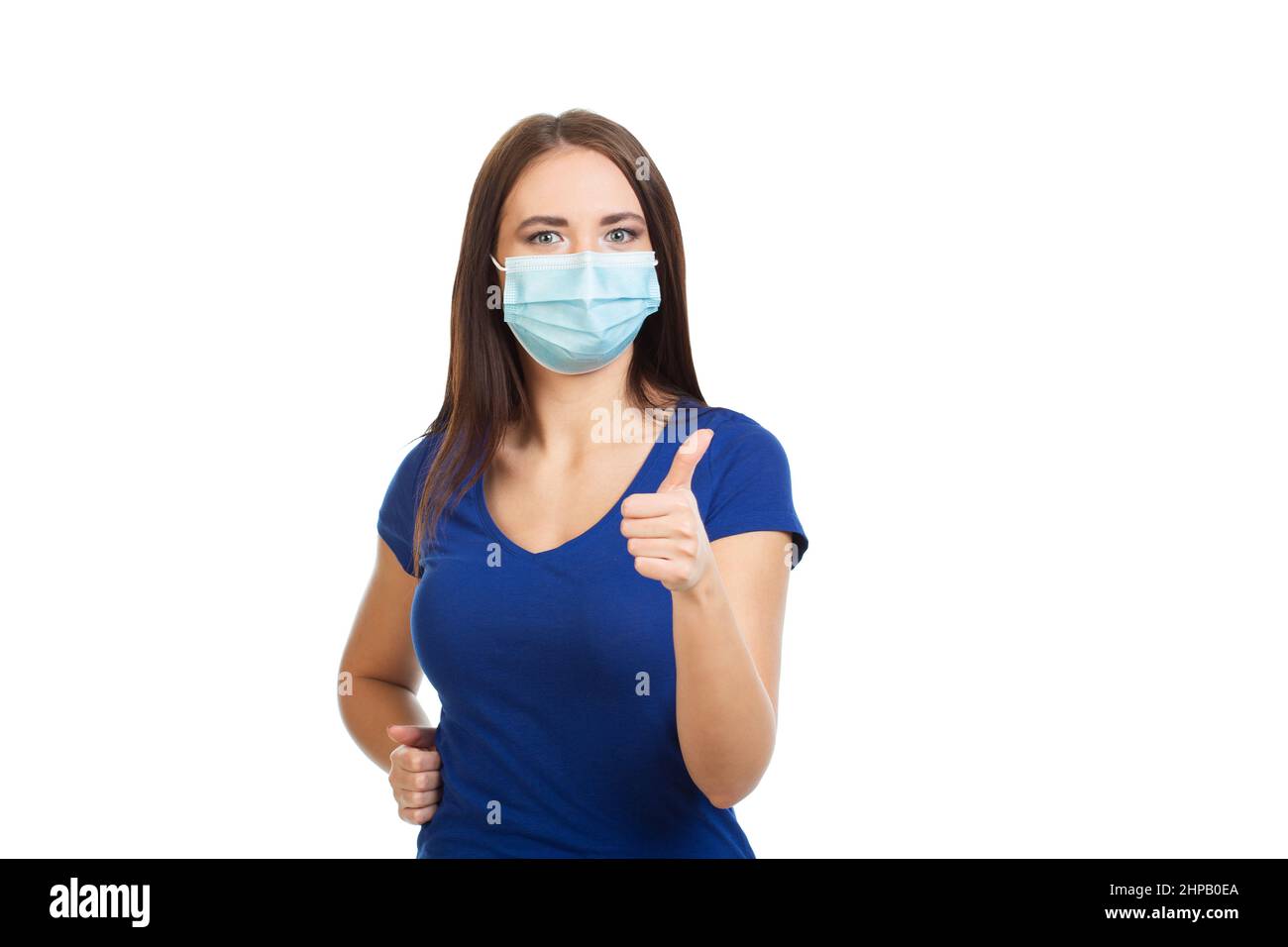 Girl in a medical mask shows a thumbs up gesture. Isolated on a white background. Stock Photo