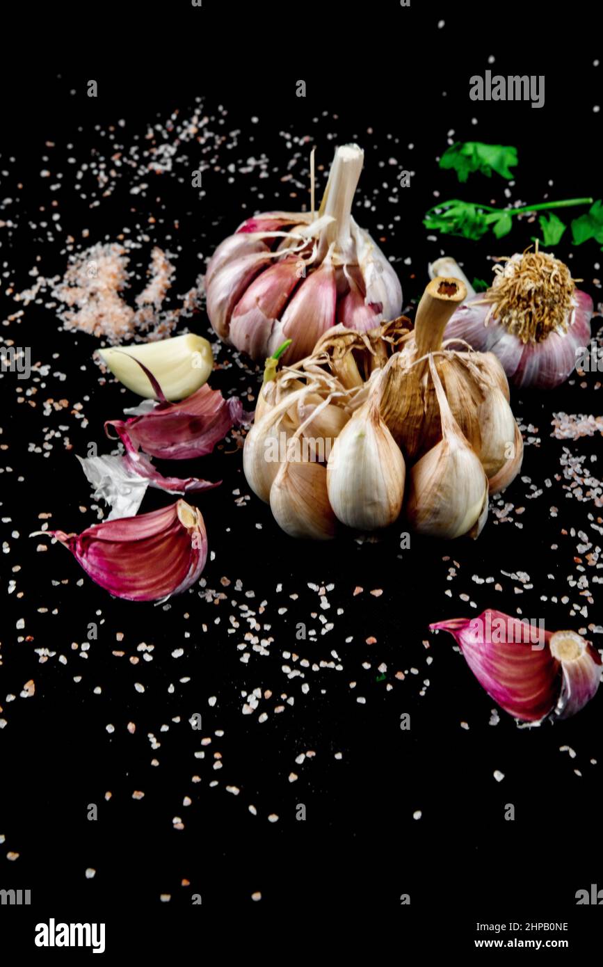 Whole and clove garlic on black background sprinkled with pink salt. Stock Photo