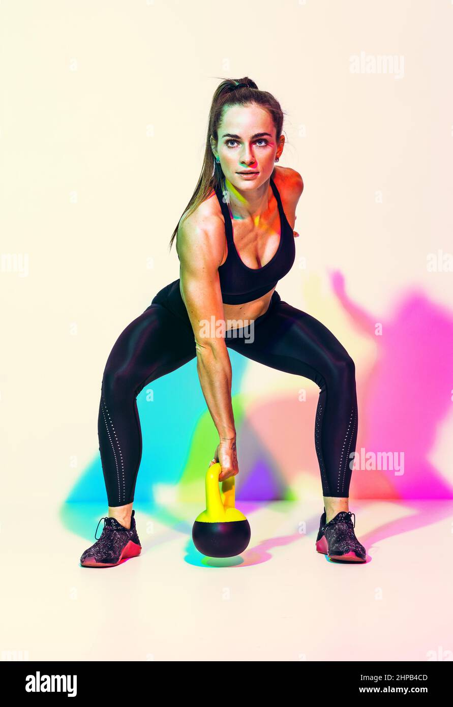 Sporty woman ready to swing the kettlebell up. Photo of woman in black sportswear on white background with effect of rgb colors shadows. Strength and Stock Photo