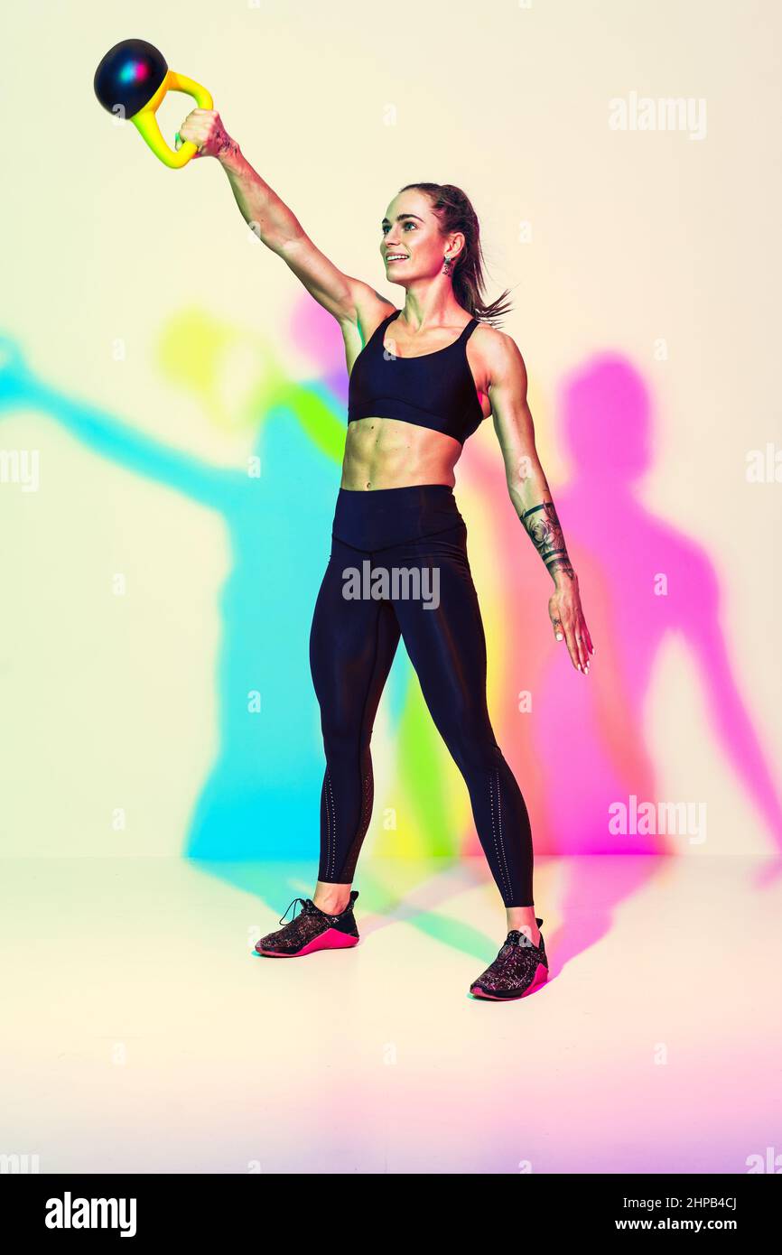 Strong woman swinging a kettlebell. Photo of sporty woman in black sportswear on white background with effect of rgb colors shadows. Strength and moti Stock Photo