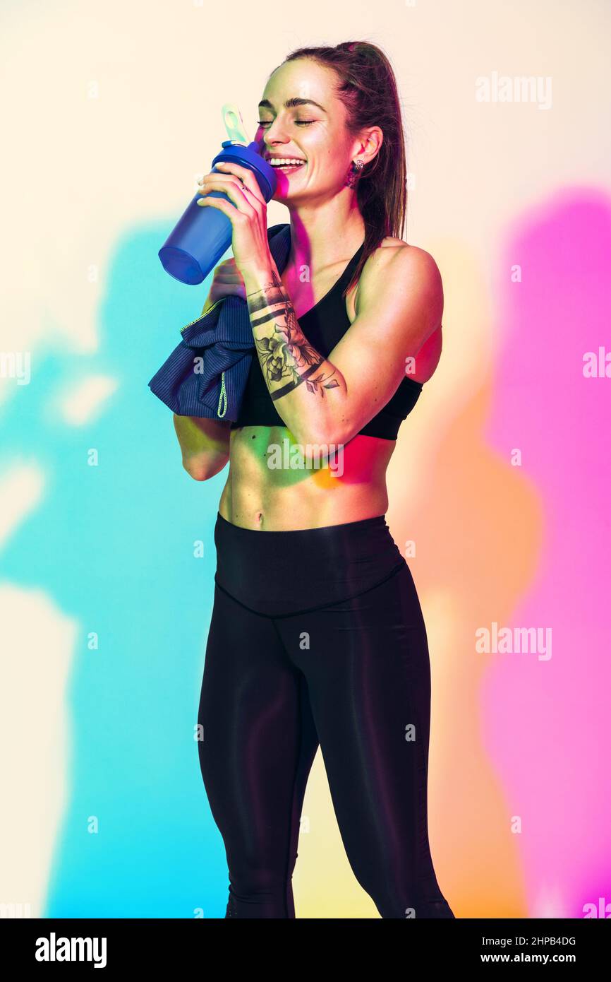 Resting time. Sporty girl with towel on shoulder drinks water. Photo of muscular woman in black sportswear on white background with effect of rgb colo Stock Photo