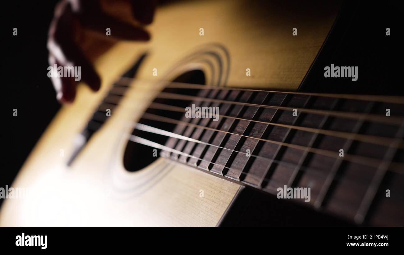 Musician enjoys playing acoustic guitar sitting in dark room. Hand of