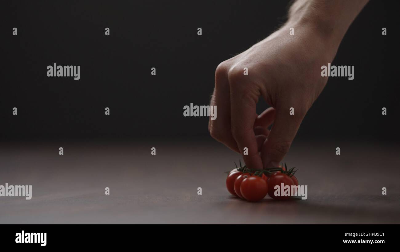man put cherry tomatoes on a bracnh on wood table, wide photo Stock Photo
