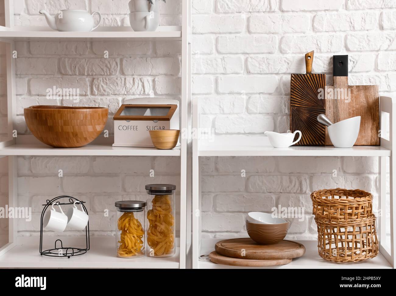 Modern shelf units with kitchenware near white brick wall Stock Photo