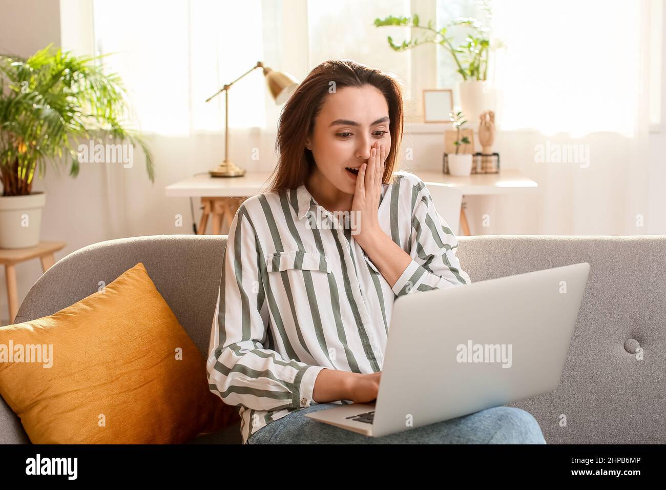 Shocked woman with laptop reading email message on sofa in light room