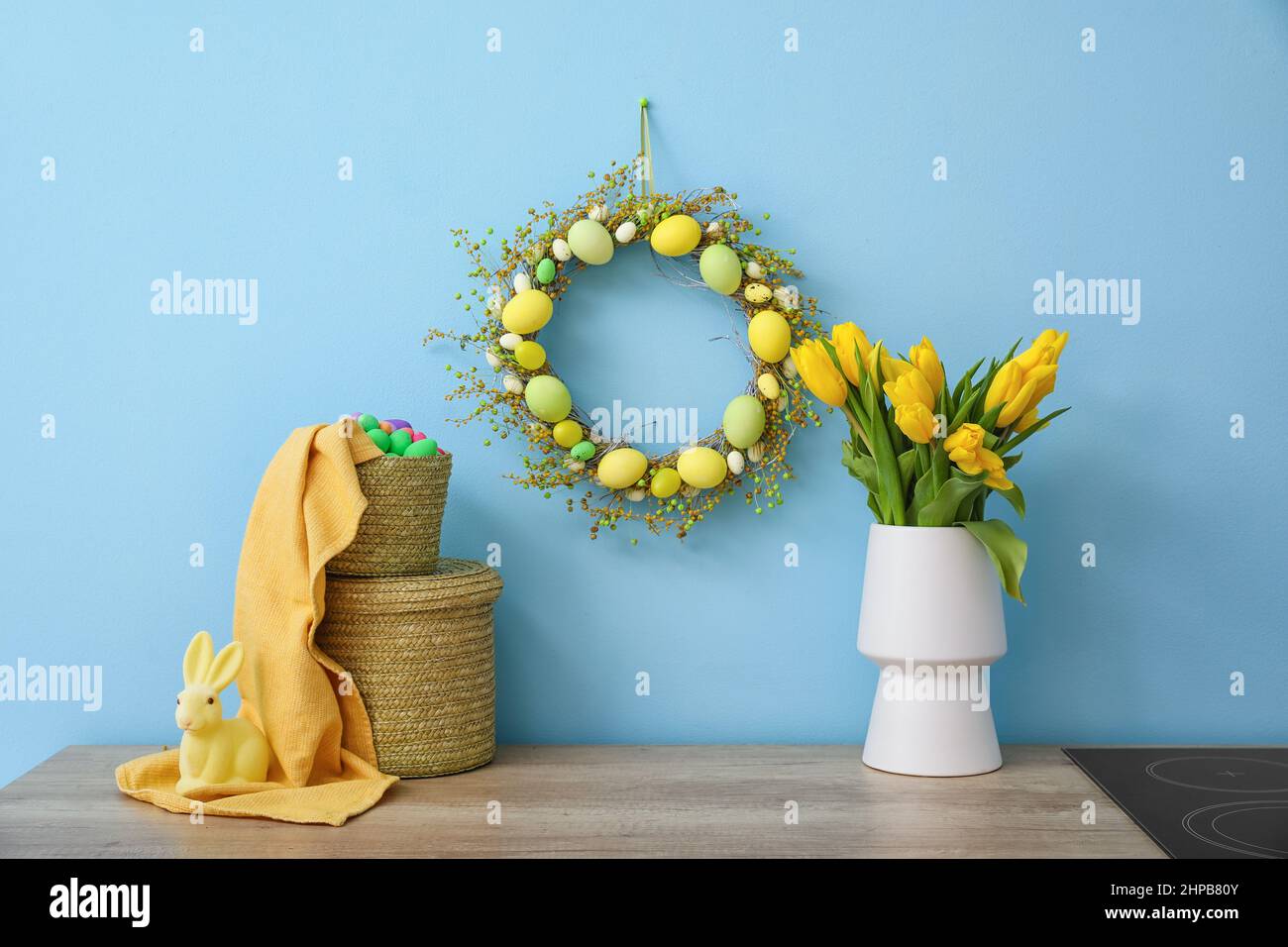 Easter wreath, basket with eggs and tulips on table near color wall ...