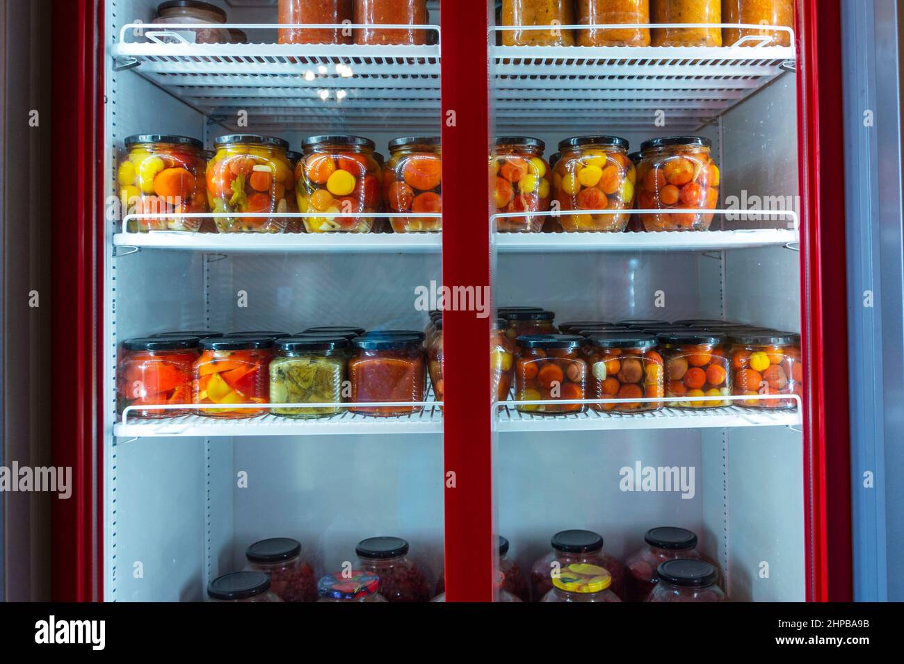 A refrigerated display case with cans of canned home products, a refrigerator with canned fruits and vegetables. Food storage. Stock Photo