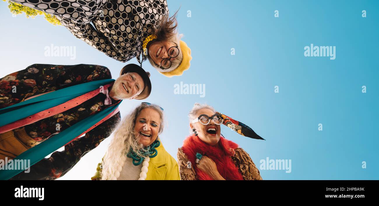 Low angle view of cheerful elderly people laughing with joy outdoors. Group of carefree elderly people wearing colourful casual clothing. Happy senior Stock Photo