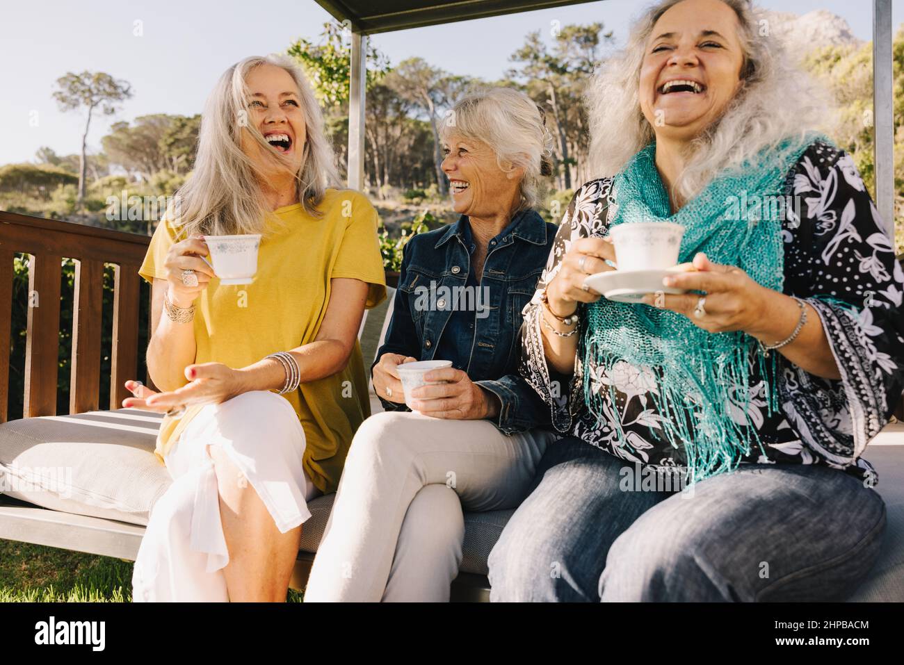 Senior women laughing happily while having tea together. Group of elderly friends enjoying their summer vacation at a spa resort. Three mature women e Stock Photo