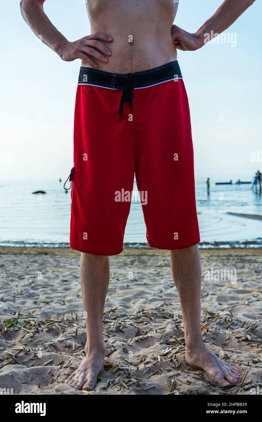 a thin tall man in red bathing shorts on the beach on a hot sunny day. Stock Photo