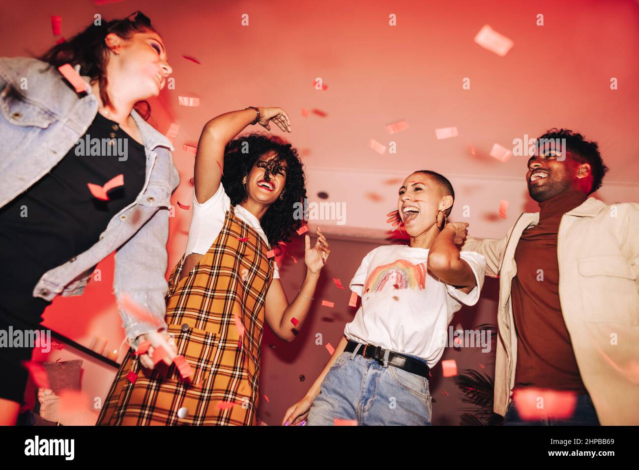 Enjoying the life of the party. Group of happy friends dancing to their favourite song under falling confetti. Multicultural friends having fun at a v Stock Photo