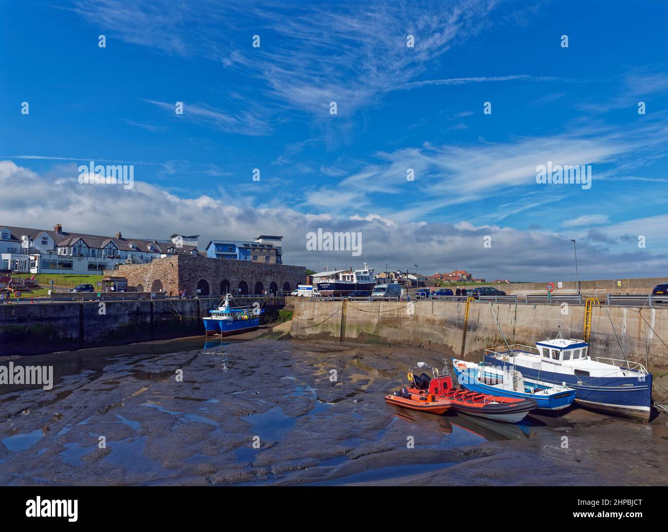 North Sunderland harbour at Seahouses at Low Tide, with Boats resting on the silty bottom of the Harbour, overlooked by Houses and Commercial Building Stock Photo