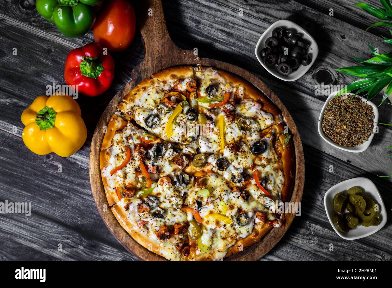 Top shot of a baked pizza and some jalapenos and olives in plates Stock