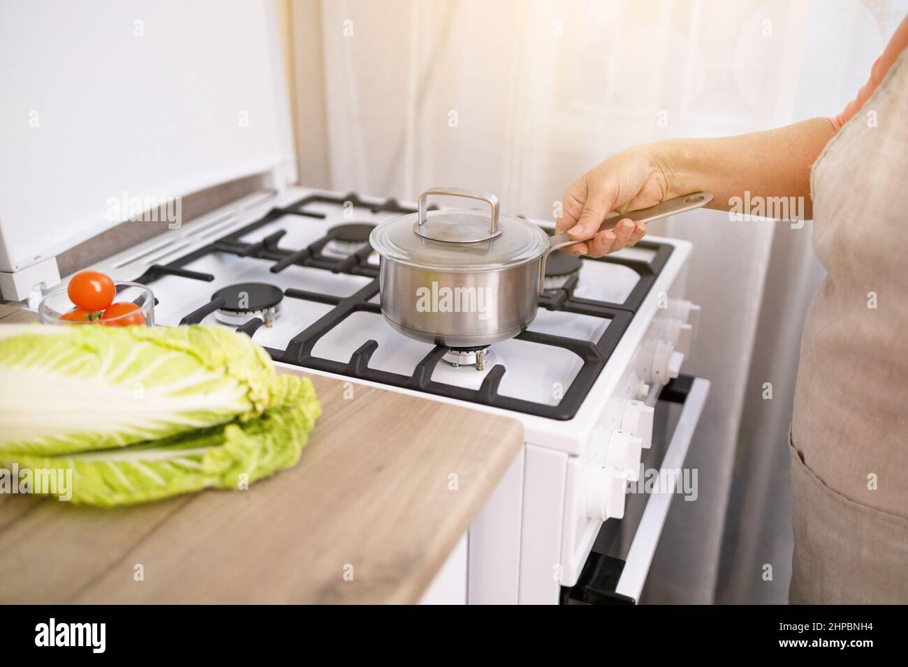 Woman puts stainless steel pot on gas stove in modern kitchen. Cooking