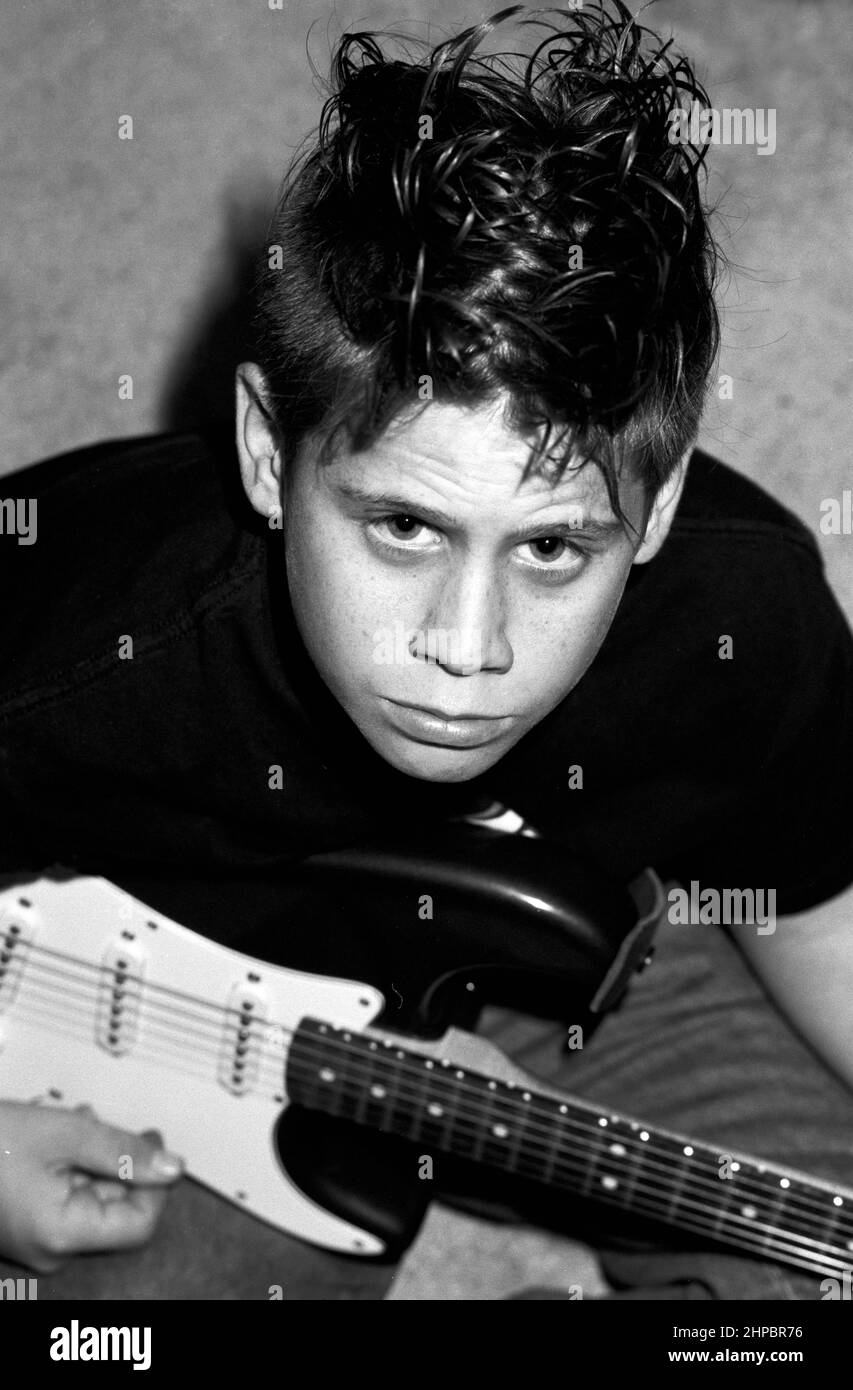 Stock image of a male teen with spiked Mohawk hair style playing a guitar, photo in black and white. Stock Photo