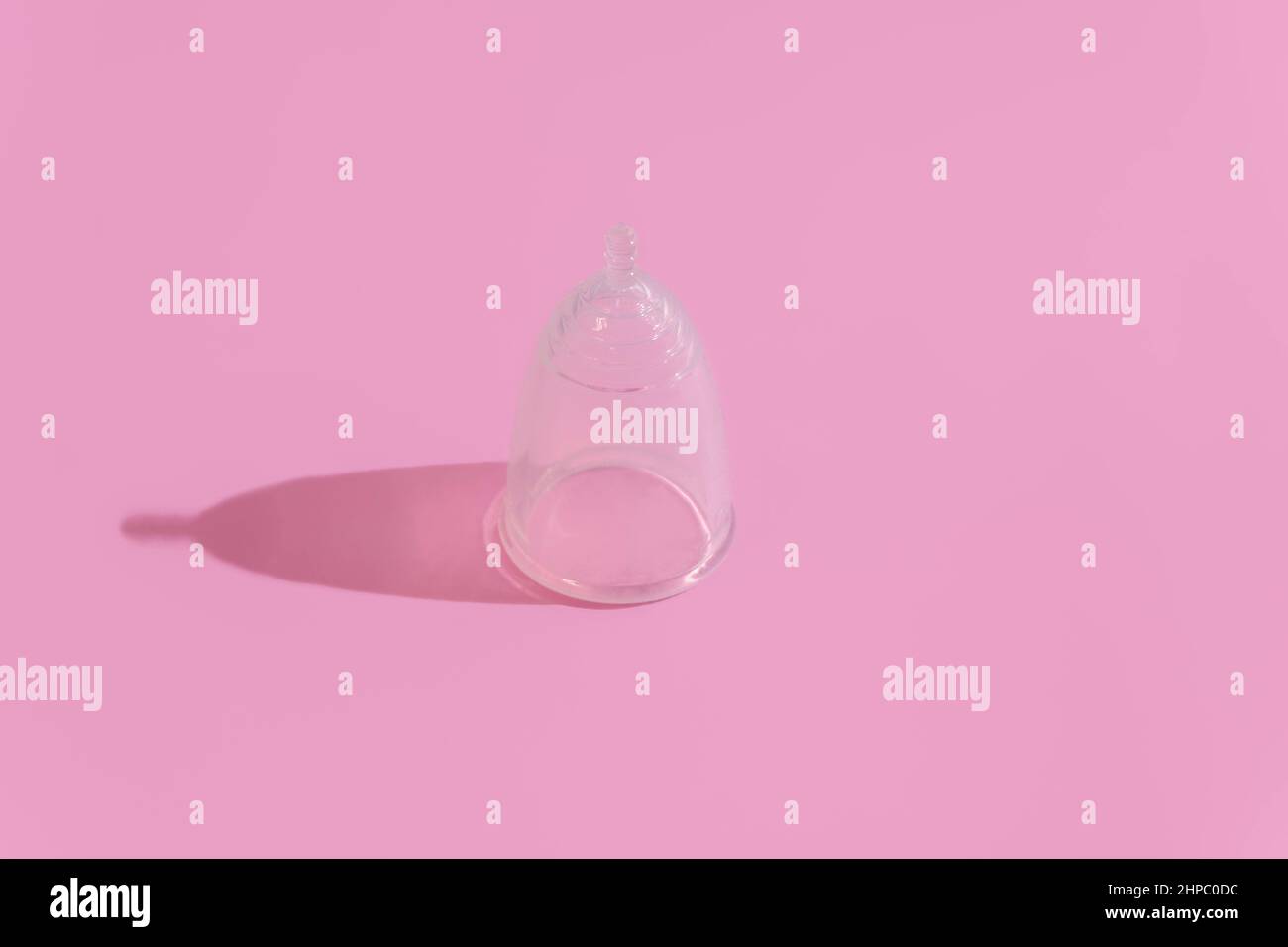 Silicone menstrual cup on soft pink background with hard shadow and space for text Stock Photo