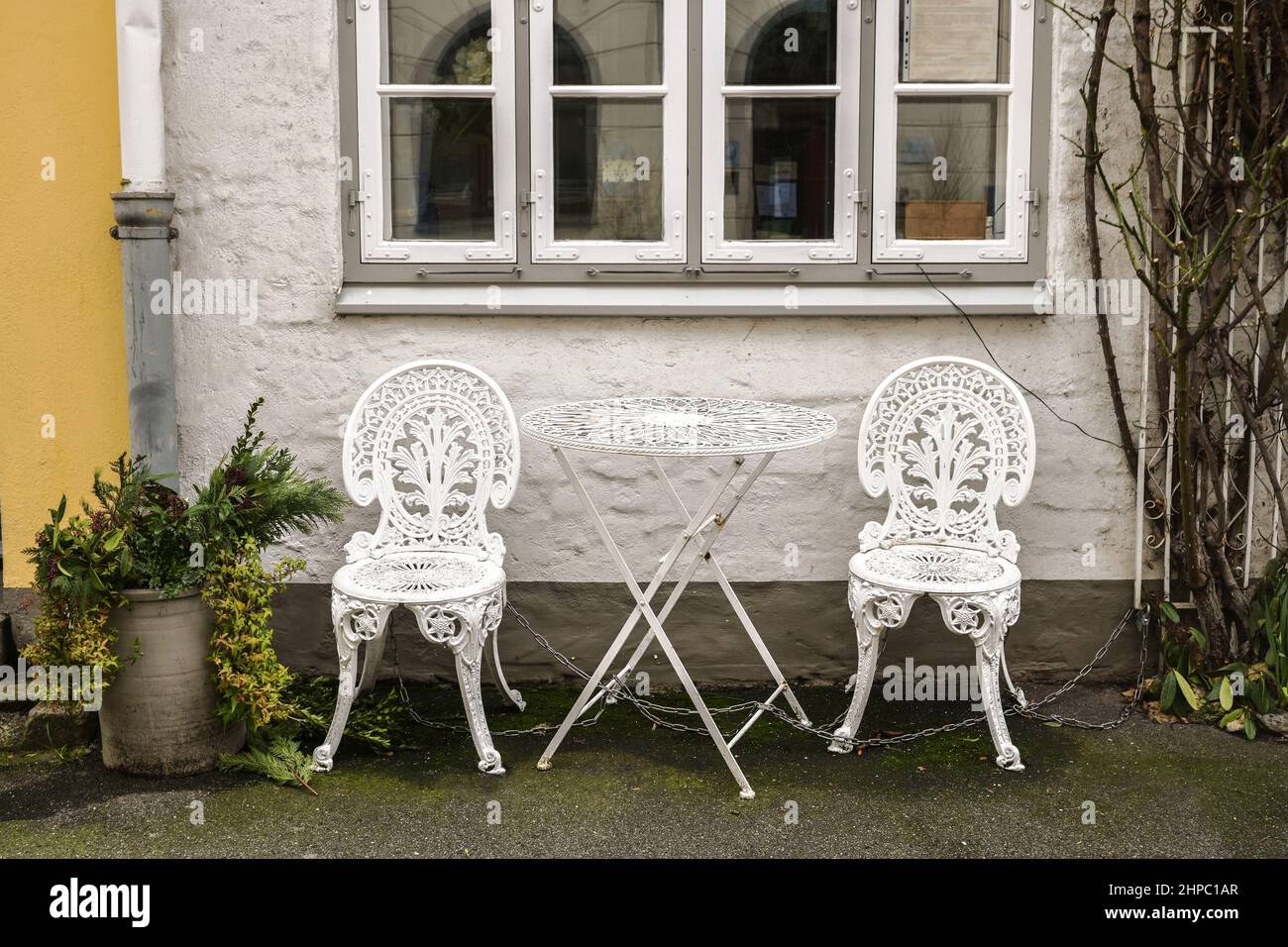 White painted iron chairs and a folding table with decorative vintage ornaments on the sidewalk in front of a historic house facade in the old town of Stock Photo
