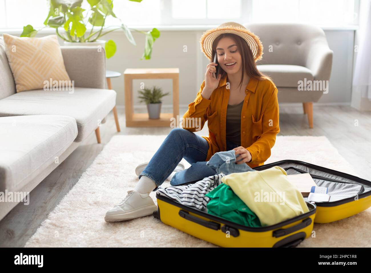 Cool woman sitting near suitcase, speaking on cellphone, booking travel tour, making hotel reservation or buying tickets Stock Photo
