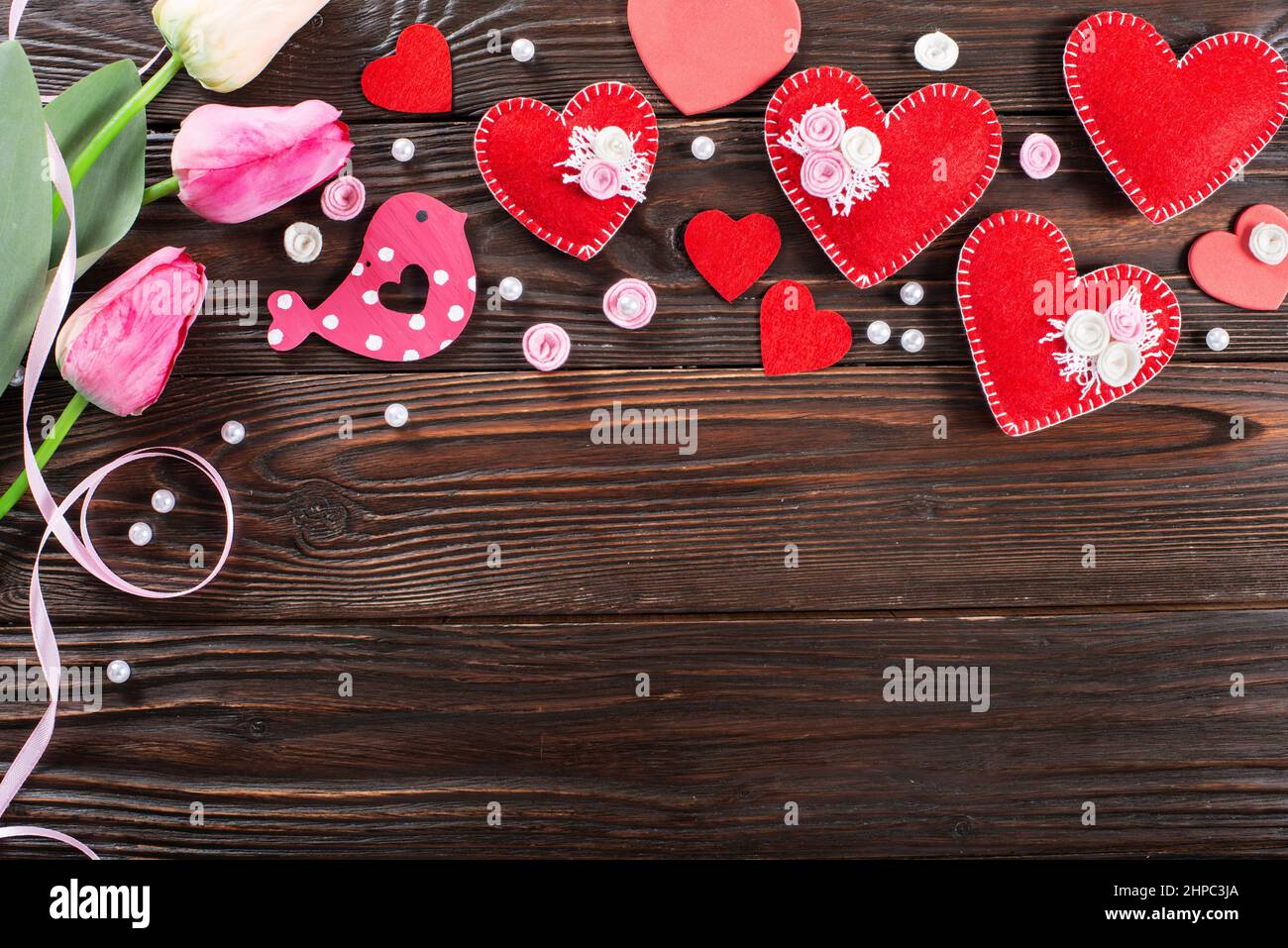 Sewed handmade fabric hearts tulips and ribbon for valentine day on dark wooden background with copy space Stock Photo
