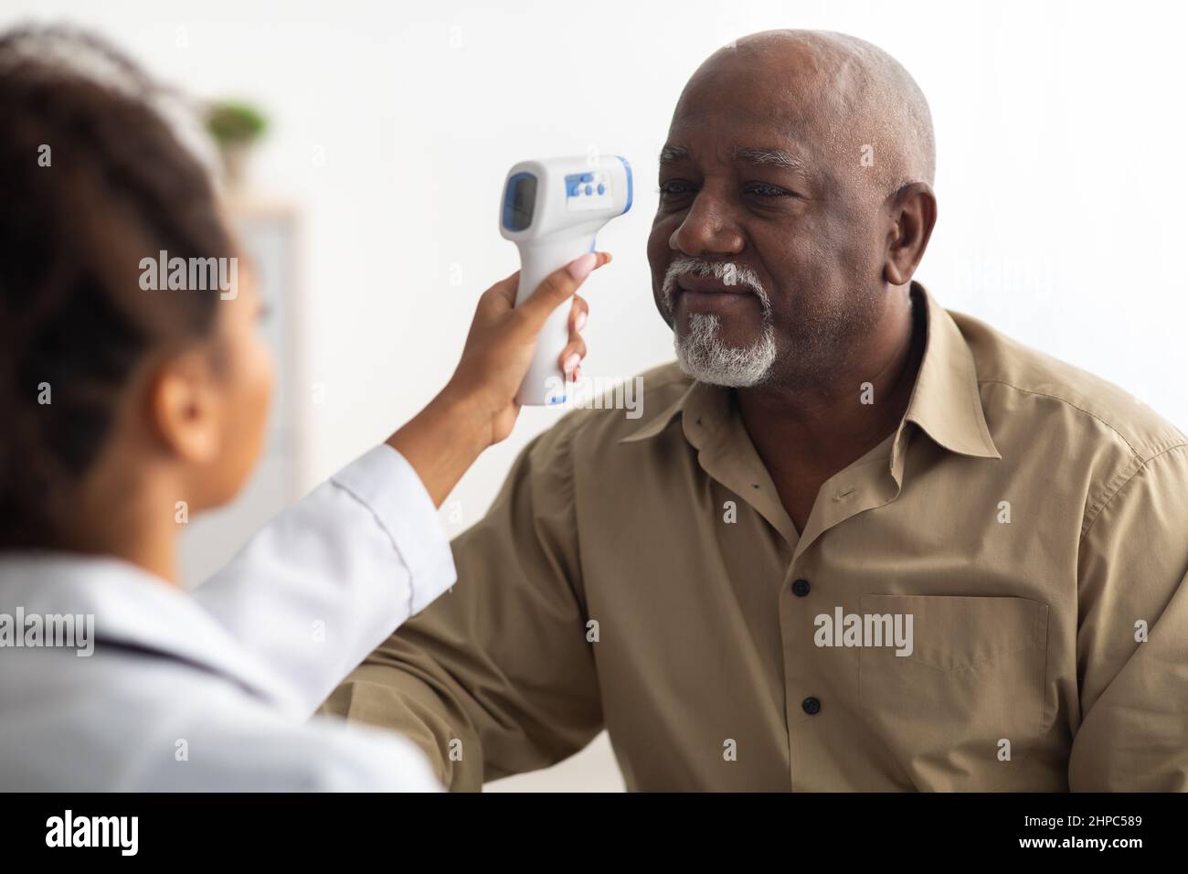 Doctor checking temperature of old man using infrared thermometer Stock