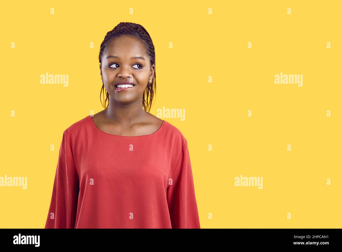 Portrait of cute and funny unsure african american woman biting her lip on yellow background. Stock Photo