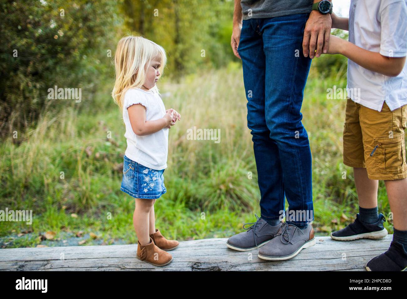 Young toddler girl, upset looking at tall daddy's legs Stock Photo